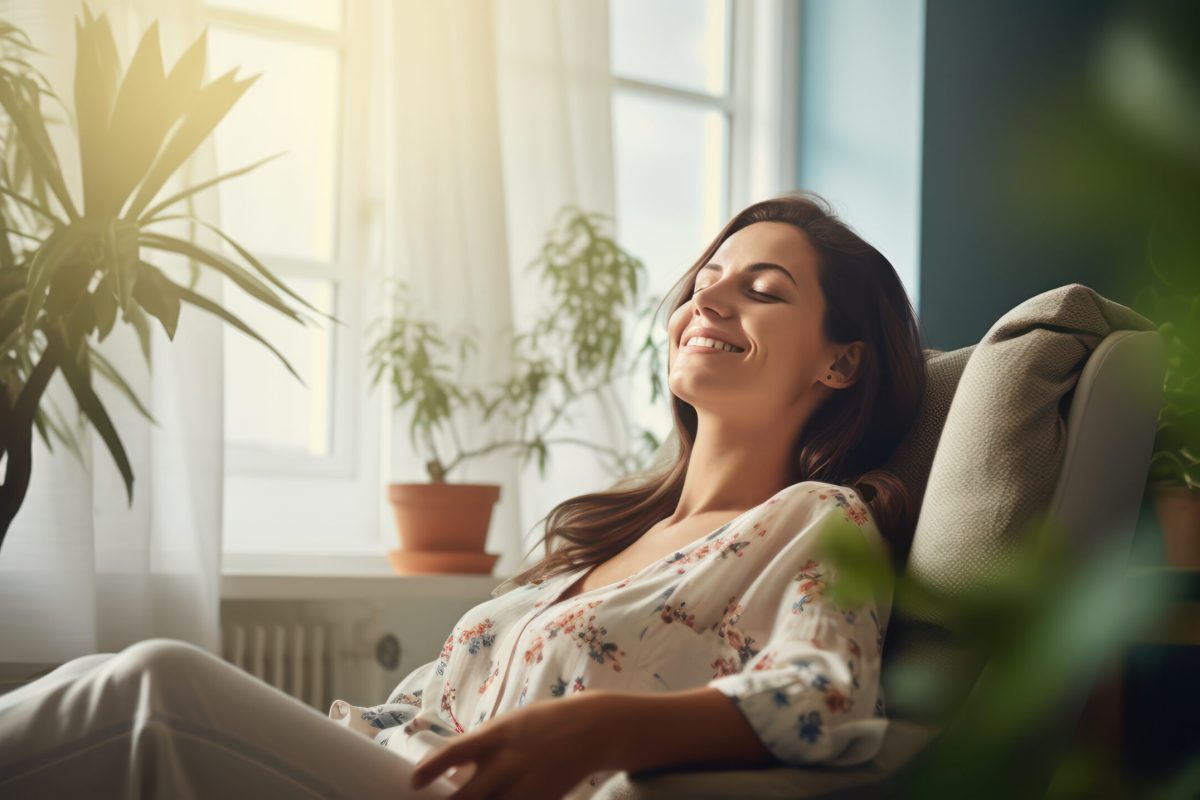 A Happy woman sitting in comfortable chair in home design, relaxing, breathing fresh air. A smiling young female tenant or a tenant relaxing in an armchair relieves negative emotions